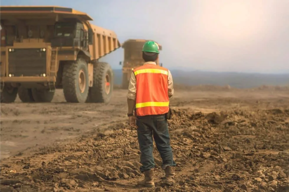 Worker in hi-vis at a mine site with haul trucks